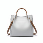 Gray handbag with brown handles and strap on a wooden surface