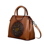 Brown leather handbag with decorative emblem on a dark background