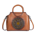 Brown leather handbag with decorative circular emblem on a white background