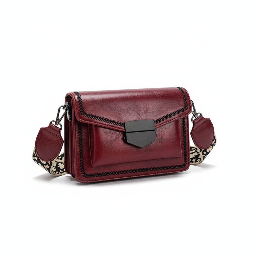 Red handbag with a patterned strap on a beige blanket