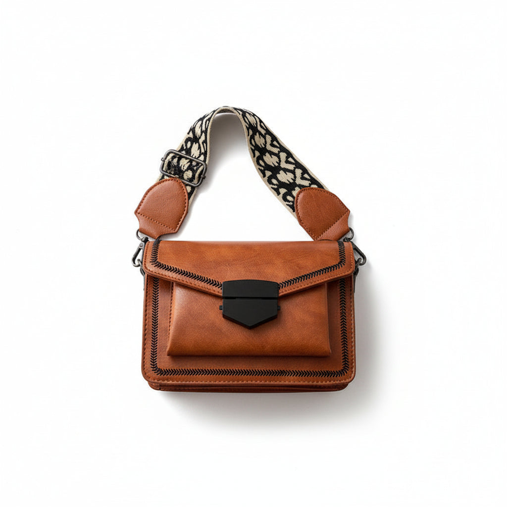Brown leather handbag with patterned strap held by a hand on a light background
