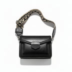 Black handbag with a patterned strap held by a hand on a light background