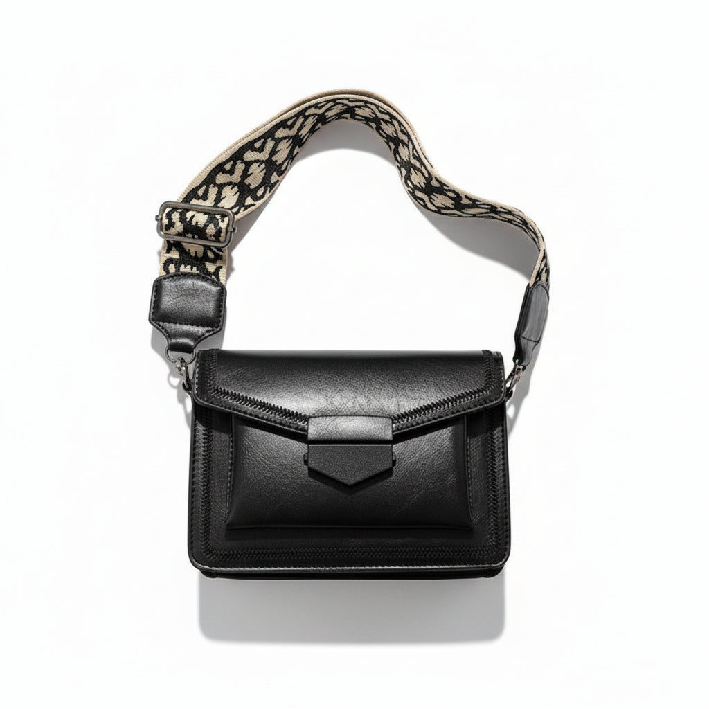 Black handbag with a patterned strap held by a hand on a light background