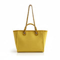 Yellow handbag with gold chain straps hanging on a coat rack against a neutral wall.
