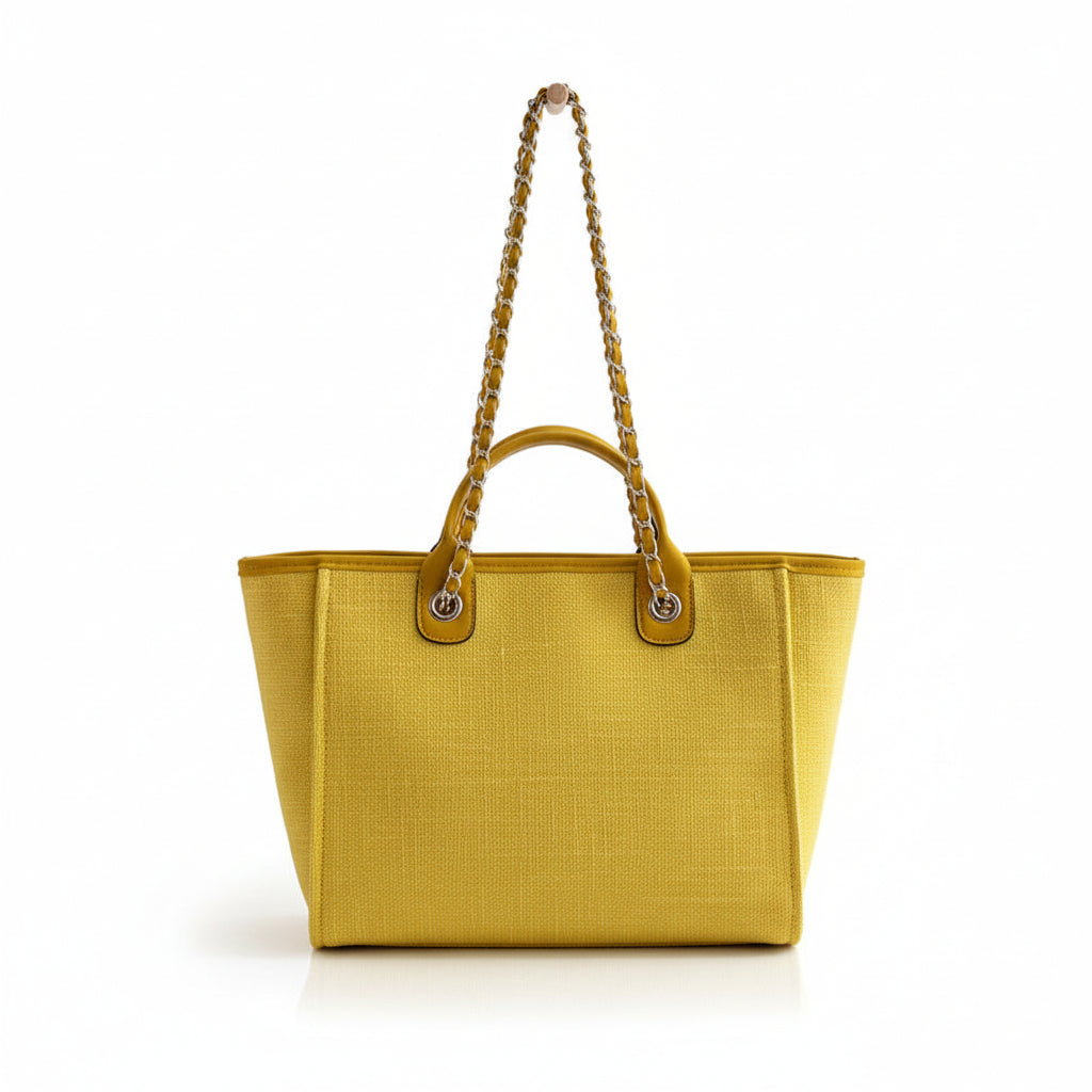 Yellow handbag with gold chain straps hanging on a coat rack against a neutral wall.
