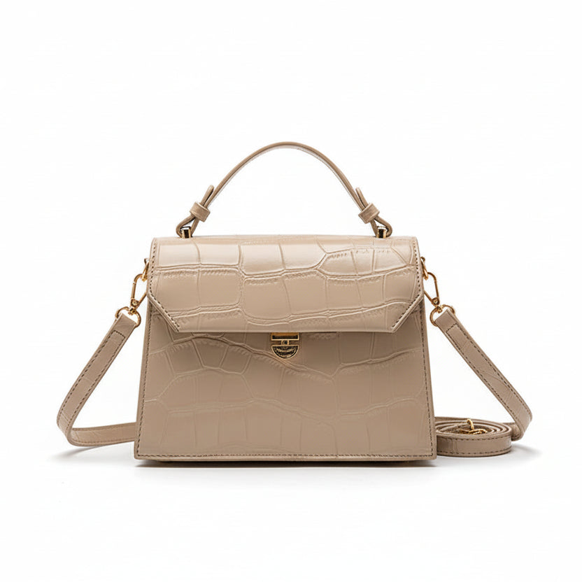 Beige crocodile-patterned handbag held by a person with a blurred indoor background