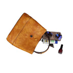 Brown leather clutch bag with items like money, sunglasses, and a phone on a gray surface.