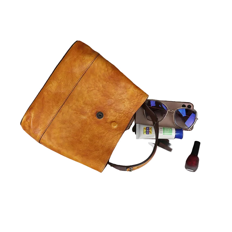 Brown leather clutch bag with items like money, sunglasses, and a phone on a gray surface.