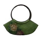Green handbag with floral designs on a textured brown background