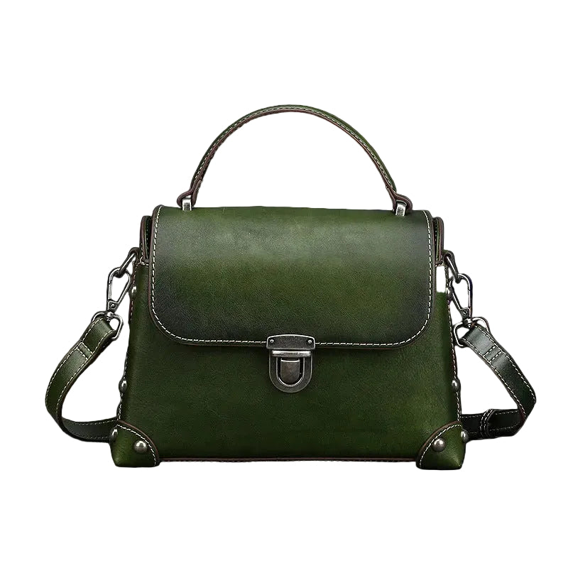 Green leather handbag with a buckle on a gray surface with decorative elements.