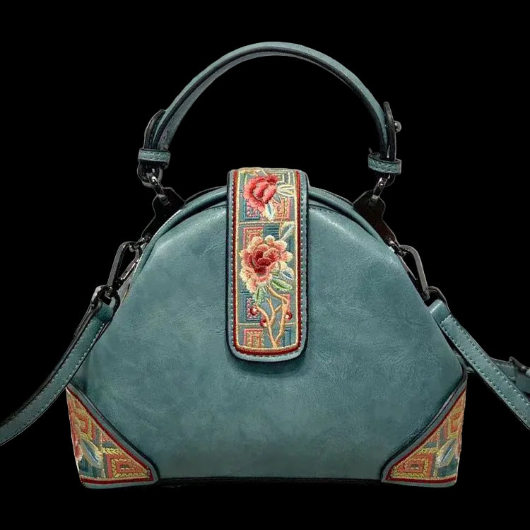 Teal handbag with floral embroidery on a neutral background
