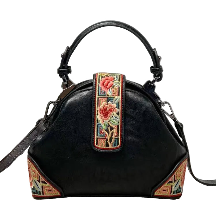 Black handbag with floral embroidery strap on a textured surface