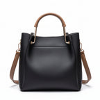 Black handbag with brown handles and strap on a wooden surface