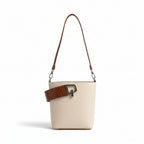 Beige handbag with brown strap and white blouse on a light fabric background