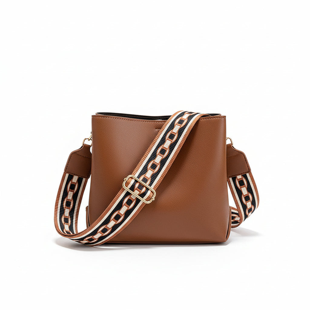 Brown leather handbag with a decorative strap held by a hand on a neutral background