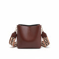 Brown leather handbag with a decorative strap held by a person on a neutral background