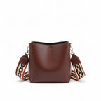 Brown leather handbag with a decorative strap held by a person on a neutral background