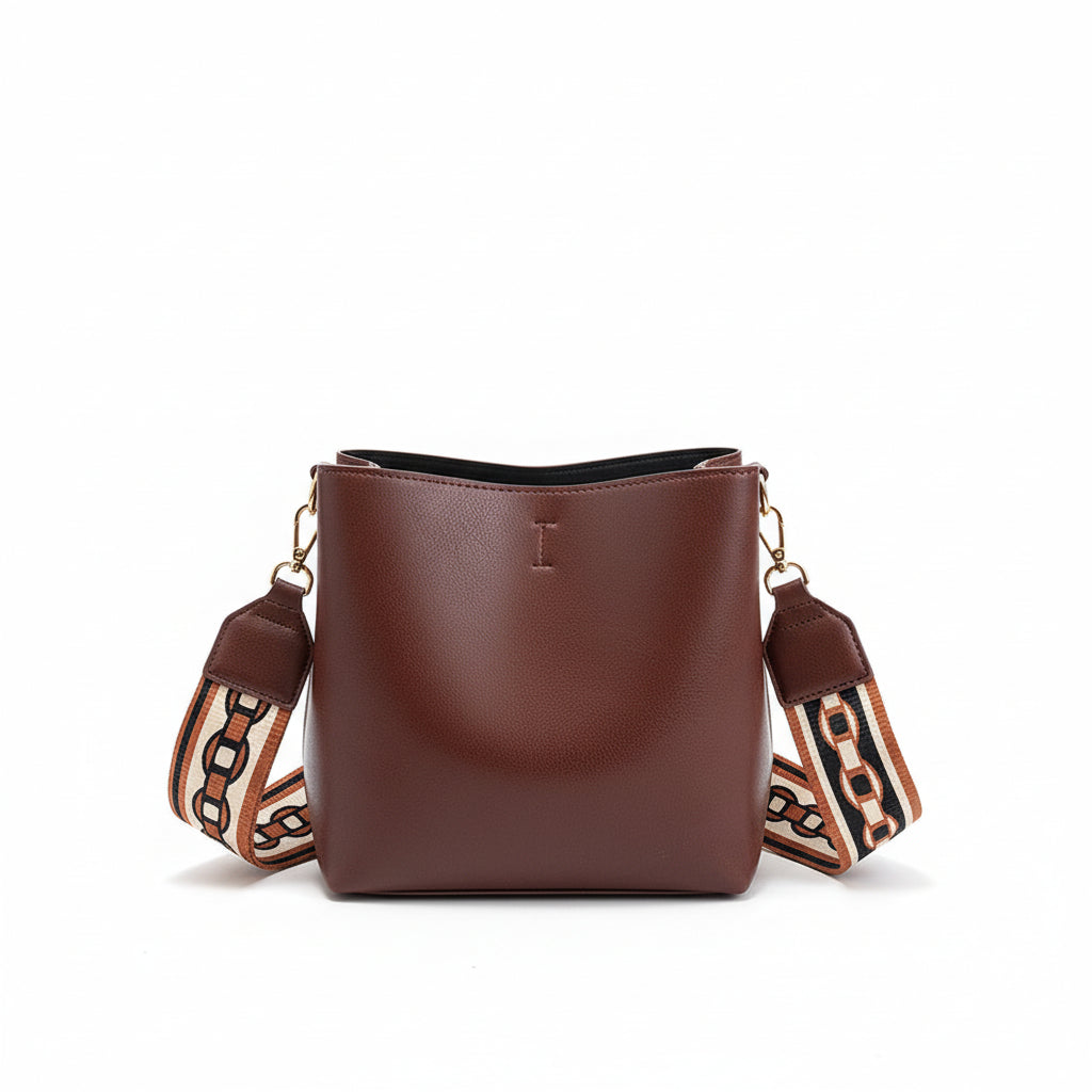Brown leather handbag with a decorative strap held by a person on a neutral background