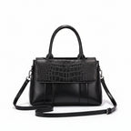 Black handbag with crocodile texture on a white surface with a brown background