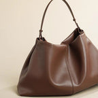 Brown leather handbag on a beige surface with a magazine underneath