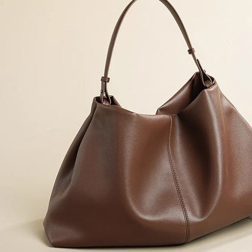 Brown leather handbag on a beige surface with a magazine underneath