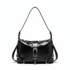 Black leather handbag held by a person against a neutral wall.