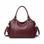 Brown leather handbag with zippers on a beige background