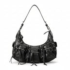Black leather handbag with multiple zippers held by a hand on a light gray background